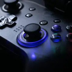 Gra w cieniach. Kontroler do gier z niebieskim podświetleniem i błyszczącymi przyciskami, tworzący magiczny shadowplay.